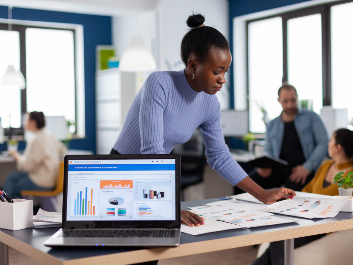 African entrepreneur of start up company reading charts on documents paperwork. Diverse team of business people analyzing company financial reports from computer. Successful corporate professional entrepreneur online internet statistics
