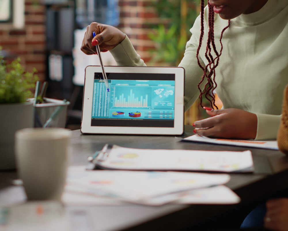 Diverse team of people analyzing data charts report on digital tablet, using online networking information to plan business project. Colelagues looking at diagrams and infographics. Close up.