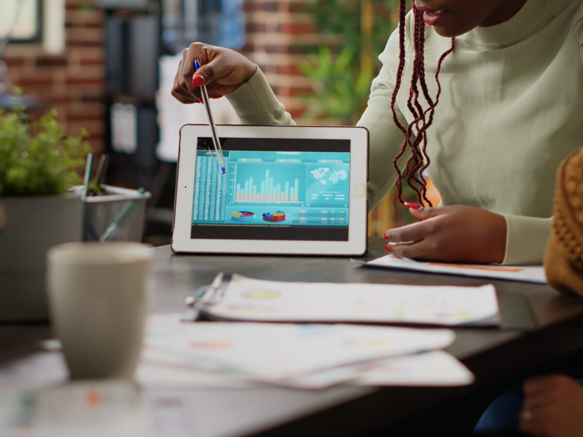 Diverse team of people analyzing data charts report on digital tablet, using online networking information to plan business project. Colelagues looking at diagrams and infographics. Close up.