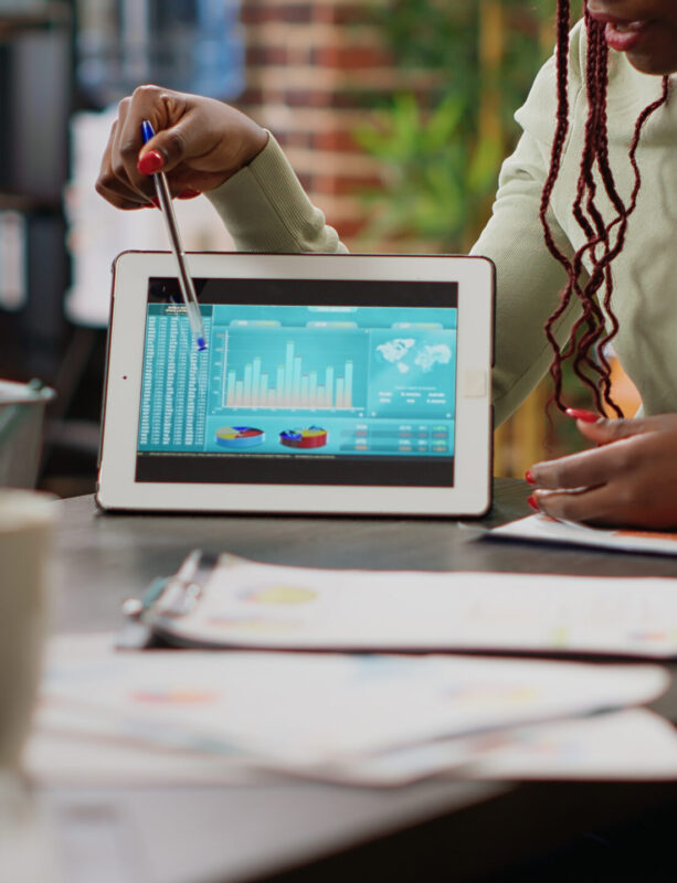 Diverse team of people analyzing data charts report on digital tablet, using online networking information to plan business project. Colelagues looking at diagrams and infographics. Close up.